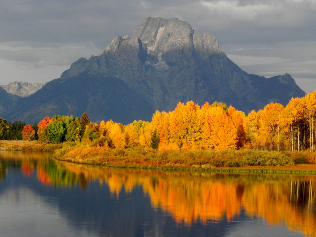 autumn trees reflecting in calm lake beneath mountain peak